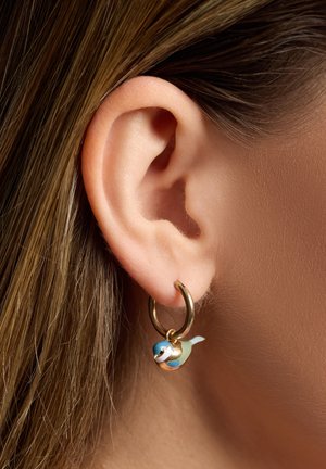 Pendiente de aro dorado con un pequeño charm de pez colorido; el pez presenta detalles en azul claro, blanco y negro; textura suave.