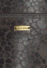 Mörk texturerad tyg med oregelbundet pebble-liknande mönster och en liten rektangulär guldmetallmärke fäst med sömnad.