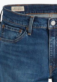 Jeans de denim azul con un ajuste clásico, que cuentan con remaches de cobre, un cierre de botón en la parte delantera y una etiqueta de cuero en la cinturilla.