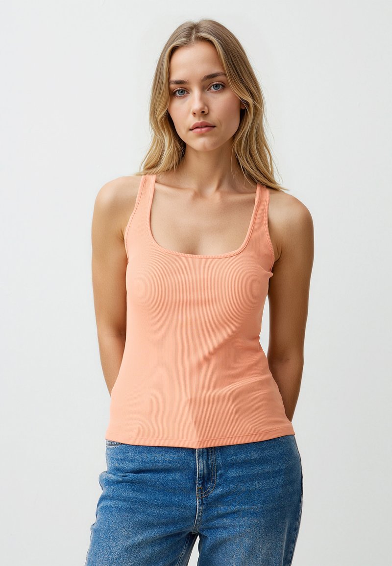 Rippenträgershirt in Pfirsichtönen mit eckigem Ausschnitt und breiten Trägern, kombiniert mit blauen High-Waist-Jeans aus Denim. Glatte Textur und figurbetontes Design.
