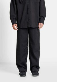 Zwarte gestructureerde shirt met zichtbare knoopsluiting en zak, gecombineerd met bijpassende wijde broek. De stof heeft een geribbelpatroon.