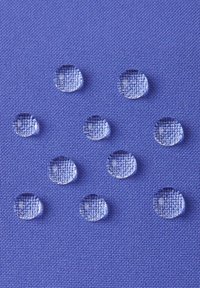 Niebieska teksturowana tkanina z wyraźnymi kroplami wody, różnymi pod względem wielkości, równomiernie umieszczonymi na powierzchni, podkreślającymi właściwości materiału.