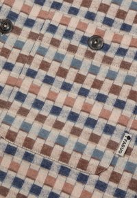 Patroonstof met lichte beige, blauwe en bruine vierkanten. Twee zwarte knopen zijn zichtbaar aan de voorkant. Inclusief een merketiket aan de zijkant.