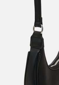 Sort læderhåndtaske med rem forbundet til en sølvfarvet metalring med synlige syninger og lynlåsdetailler på taskens krop.