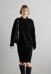 Un sweat noir surdimensionné avec un décolleté en V, superposé à une chemise noire à col, assorti à une jupe noire ajustée et des bottes noires jusqu'aux genoux.