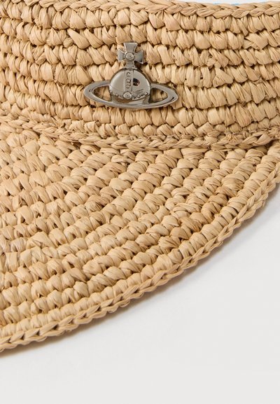 Κοντινό πλάνο μπεζ πλεγμένου ψάθινου καπέλου με ένα μικρό ασημένιο σφαίρα και σταυρό, τοποθετημένο κοντά στην άκρη της γείσο.