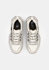 White athletic shoes with multi-textured panels, thick soles, and reflective accents. Features prominent lacing system and logo on insoles.