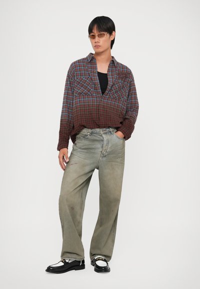 Rood en blauw geruite oversized shirt, zwarte tanktop, vervaagde groene wijde jeans, zwarte schoenen met een kettingaccent, versleten textuur.