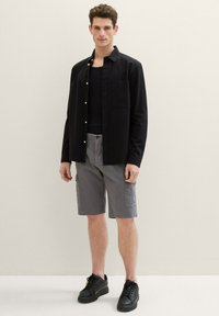 Black button-up shirt over a black tank top, gray cargo shorts, and black sneakers. The shirt has a chest pocket and relaxed fit.