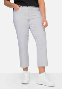 Pantaloni cropped grigio chiaro con taglio dritto, caratterizzati da un orlo grezzo e tasche frontali, abbinati a sneakers bianche alte.