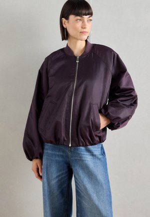 Purple bomber jacket with a zip front, ribbed collar, elastic cuffs, and relaxed fit. Paired with blue wide-leg jeans.