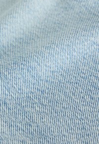 Light blue denim fabric with fine vertical white and blue woven threads and a slightly wrinkled texture.