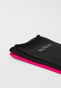 Sorte og pink ribbede sokker med "HUGO" logoet i grå, lagt fladt med sort ovenpå og pink nedenunder. Blød tekstur og glat finish.