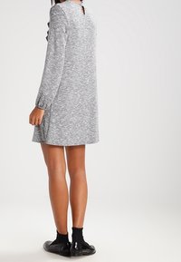 Šedé pletené šaty s dlouhými rukávy, detaily s otvorem na zádech a bočními rozparky, sahajícími nad kolena. Doplněno černými ponožkami a botami.