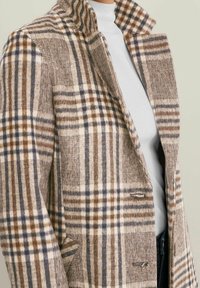 Abrigo de cuadros marrones y beige con un tejido texturizado, que presenta un collar en pico y un cierre de doble botonadura con acentos metálicos.