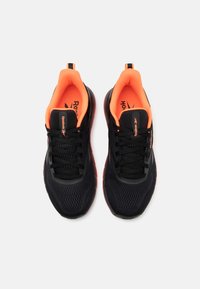 Sorte athletic sko med en åndbar mesh-overdel, orange detaljer indeni, polstret krave og sorte snørebånd. Har en tekstureret sål for bedre greb.