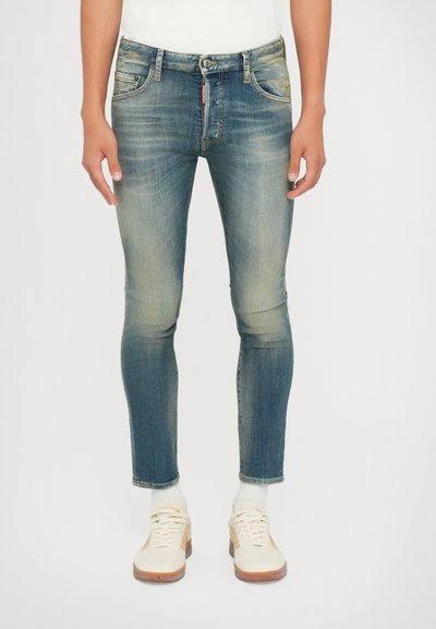 Jeans in denim blu skinny-fit con dettagli sbiaditi, cinque tasche e passanti per cintura, abbinati a sneakers bianche basse e calzini leggeri.