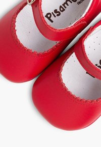 Zapatos Mary Jane de cuero rojo con un diseño de borde festoneado, puntera redonda y correa ajustable. Forro interior blanco con detalle de marca.