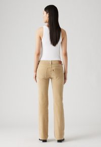Beige kordfløyelsbukser med vide beina, baklommer, Levi's-logo-lapp i midjen, og sammen med en hvit ermeløs topp.