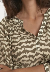 Blouse à manches longues en vert olive avec un motif abstrait crème, dotée d'un décolleté en V et d'un tissu doux et texturé.