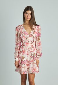 Vestido floral de tela rosa claro con grandes estampados de flores en rosa y verde, escote en V, hombros con volantes, mangas largas y detalles de botones.