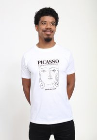 Bílá bavlněná tričko s černým konturovým nákresem hlavy dívky a texty "PICASSO" a "Hlava dívky" v hnědé barvě. Krátké rukávy.