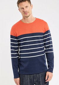 Chemise à manches longues avec une partie supérieure orange et un corps bleu marine avec des rayures blanches horizontales. Fabriquée en tissu doux et texturé.