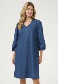 Denim jurk met een V-hals, lange pofmouwen en een losse silhouet. De stof is een lichtere blauwe kleur met een subtiele textuur en een rechte zoom.