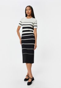Gehaakte gestreepte jurk in crème en zwart, met korte mouwen en een aansluitend design, reikt tot halverwege de kuit. Accentueert met contrasterende strepen.