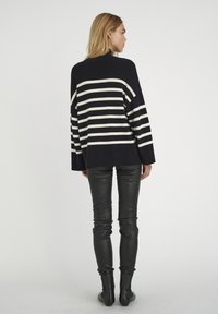Gestreifter Pullover in Schwarz und Weiß mit lässiger Passform, langen Ärmeln und weitem Ausschnitt, kombiniert mit schwarzen Lederhosen und Stiefeletten.