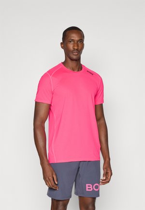 Różowa sportowa koszulka z krótkim rękawem z czarnym logo, w zestawieniu z szarymi szortami z różowym napisem. Gładki materiał, dopasowany krój i okrągły dekolt.