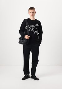 Black crew neck sweater with white graphic text, black trousers, and black shoes. A small black crossbody bag with adjustable strap.