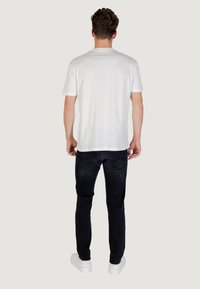 Camiseta blanca de manga corta con cuello redondo, combinada con jeans negros ajustados y zapatillas blancas, mostrando un diseño simple y sin patrones.