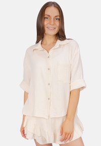 Light beige cotton shirt with a relaxed fit, short sleeves, button closure, and a chest pocket, paired with a matching ruffled skirt.