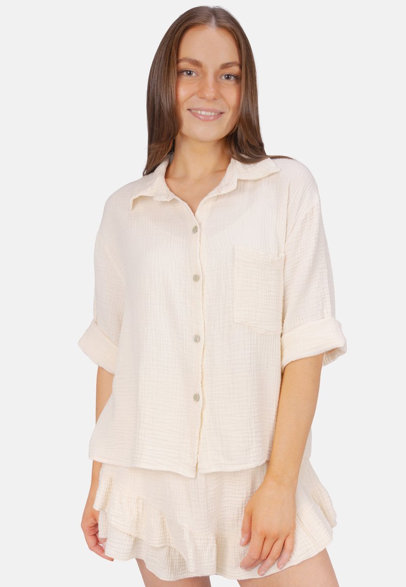 Light beige cotton shirt with a relaxed fit, short sleeves, button closure, and a chest pocket, paired with a matching ruffled skirt.