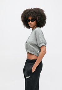 Siva skrajšana majica z zvitimi kratkimi rokavi in črnim grafičnim napisom. Ujemajoče se s črnimi trenirkami z belim logotipom.