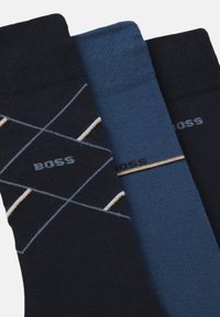 Tre paia di calzini: uno blu scuro con un motivo, uno blu uniforme e uno blu scuro con un logo. Tutti presentano polsini a coste e una consistenza morbida.