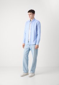 Lichtblauw overhemd met lange mouwen, gecombineerd met licht gewassen jeans en witte sneakers. Eenvoudig ontwerp, katoenen materiaal, relaxte pasvorm.