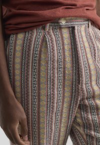Los pantalones con estampado presentan una mezcla de rayas y diseños de diamantes en tonos de rojo, amarillo, azul y blanco, con una tela sutilmente texturizada.