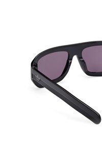 Czarnie okulary przeciwsłoneczne o kanciastym designie, fioletowe szkła, błyszcząca plastikowa oprawka oraz mały detal z logo na boku zausznika.