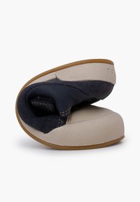 Měkká, flexibilní bačkůrka s béžovou gumovou podrážkou, tmavě modrým semišovým svrškem a prošívanými akcenty. Tvarovaný design pro pohodlí.