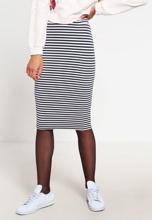 Gebreide kokerrok met horizontale zwart-wit strepen, knielang, gecombineerd met witte sneakers en doorzichtige zwarte panty's.