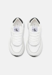 Scarpe da ginnastica bianche con tomaia in pelle liscia, dettagli grigi, parte posteriore nera e lacci bianchi spessi. Logo Calvin Klein sulla linguetta.