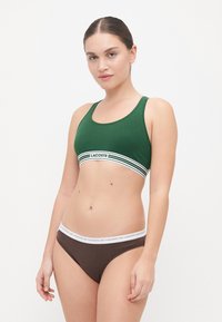 Πράσινο αθλητικό μαγιό με λευκή και πράσινη ρίγα στη ζώνη, με το λογότυπο "LACOSTE". Καφέ μπικίνι με λευκή ζώνη.