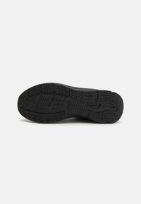Suela de zapatilla negra con una superficie de goma texturizada y un dibujo para agarre y durabilidad. Bordes suaves y contorno definido.