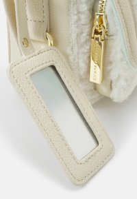 Rogaty skórzany biały zamek z teksturowanym uchwytem na metkę i złotym suwakiem z wygrawerowanym napisem "Chiara Ferragni" obok detalu z białej owczej skóry.