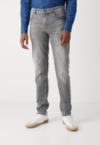 Jeans de mezclilla gris con corte ajustado y ligero desgaste. Presentan un diseño estándar de cinco bolsillos y costuras en contraste, combinados con zapatillas blancas.