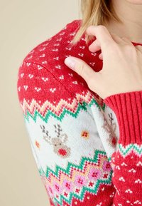 Czerwony sweter z dzianiny z białym wzorem reniferów, kwiecistymi motywami i kolorowymi zygzakowymi akcentami na mankietach i ramionach. Miękka faktura.