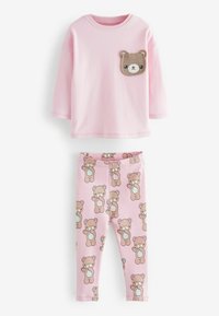 Rosa bomulls skjorta med lång ärm och en ficka i form av ett björnhuvud, parat med rosa leggings som har ett upprepat björntryck och blå ränder vid benen.