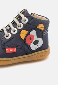 Chaussure montante en cuir bleu avec semelle en caoutchouc, présentant un design de visage de chien en plusieurs couleurs et œillets en métal pour les lacets. Marque Kickers.